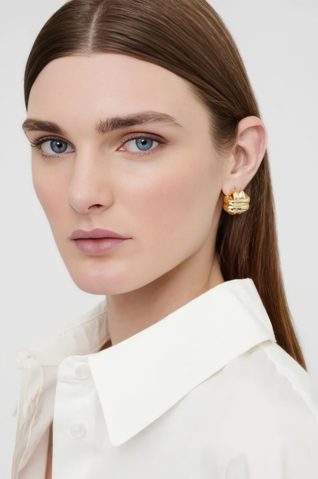 A woman wearing a white shirt and gold earrings.