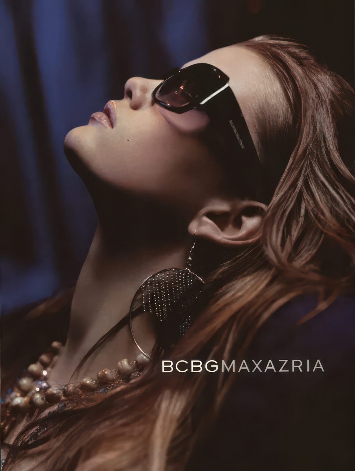 A woman with long hair wearing sunglasses and pearls.