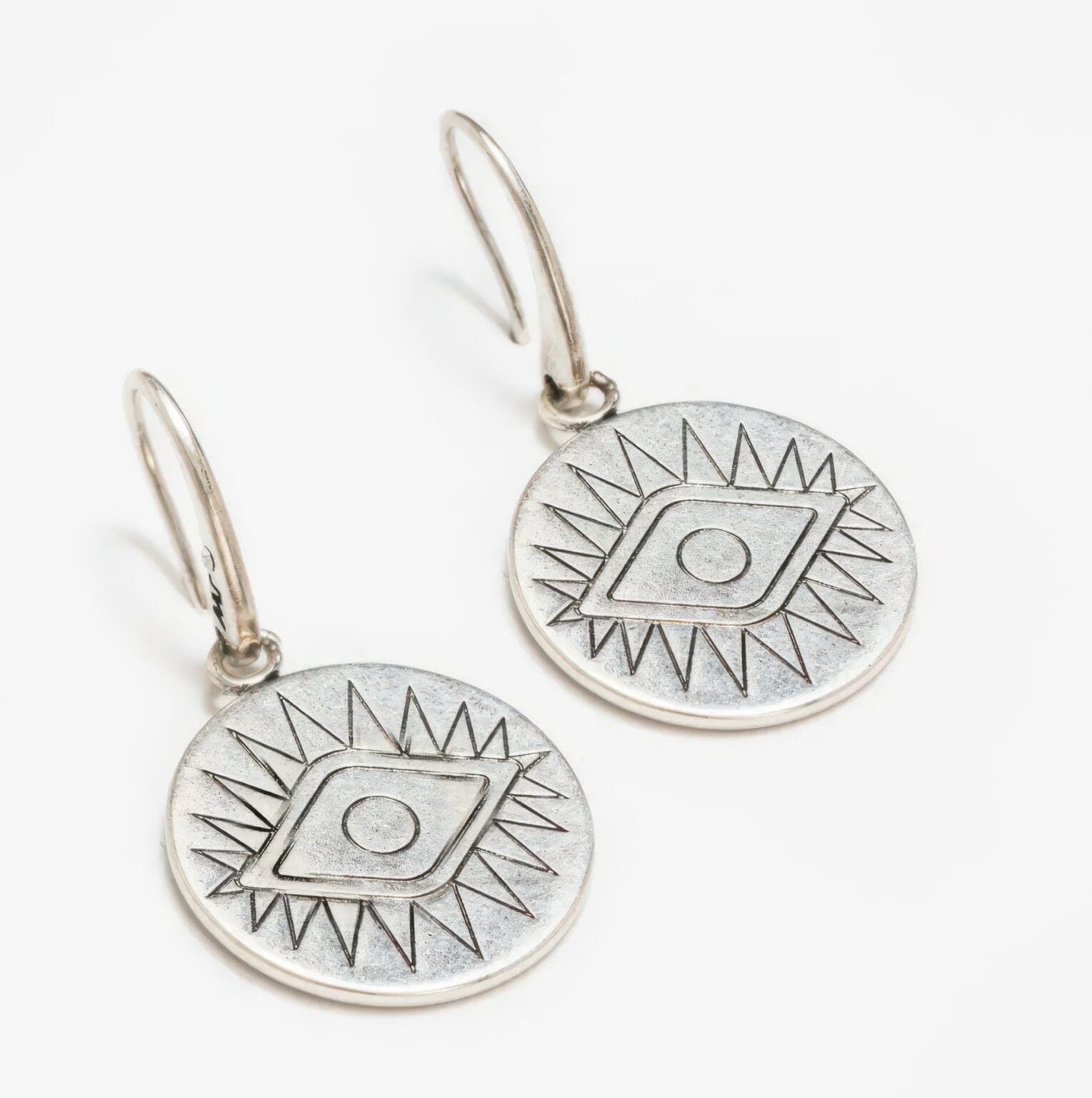 A pair of silver earrings with an eye design.
