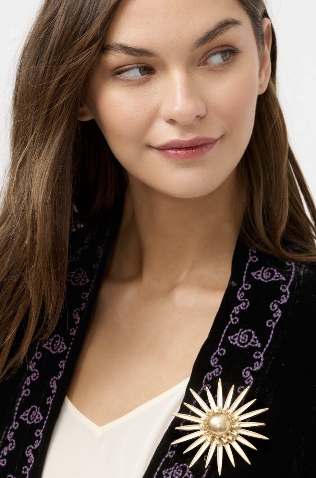 Woman wearing black jacket with sun brooch.